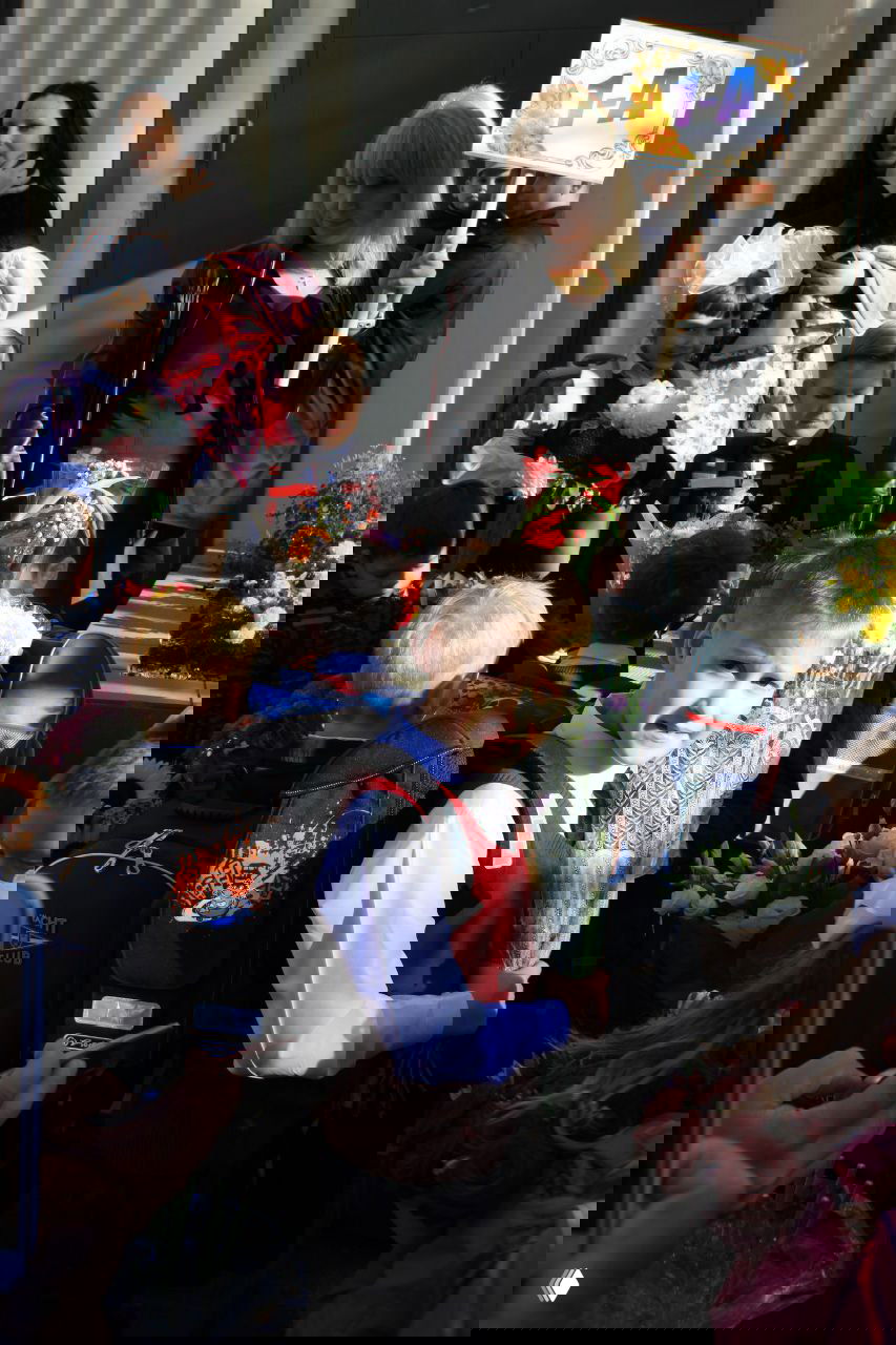 Толпа первоклассников и родителей у входа в школу: дети с букетами и табличками, праздничная атмосфера первого школьного дня.