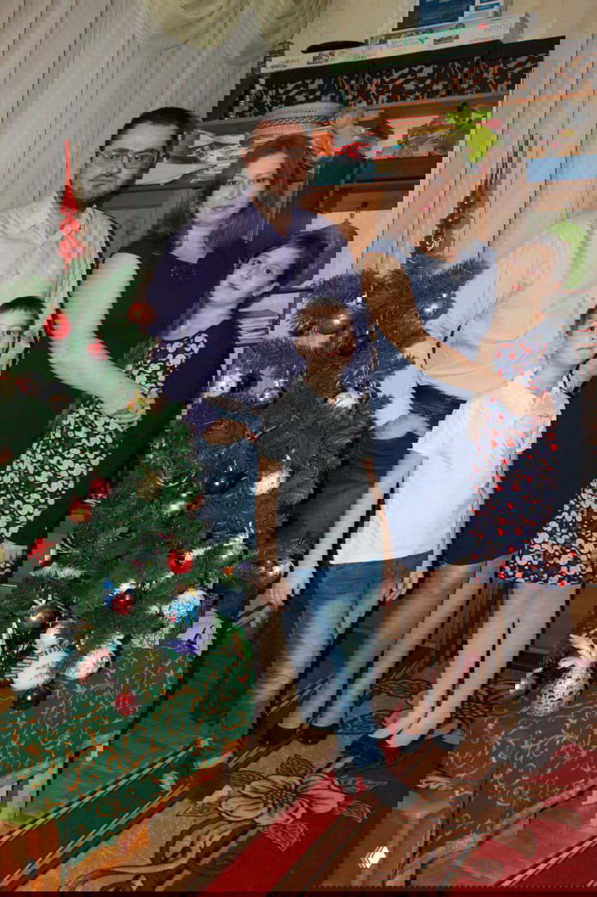 Семейная фотография у домашней елки в интерьере: родители и двое детей, праздничная обстановка и рождественские украшения.