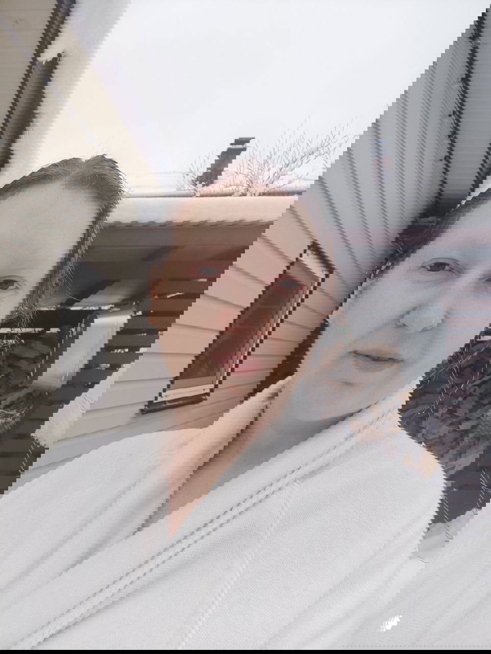 Селфи автора в белом халате на фоне снега и дровяного навеса после обливания колодезной водой; влажные волосы и спокойное лицо.