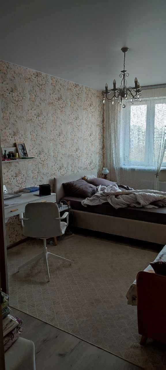 Спальная комната в нейтральных бежевых тонах: кровать, рабочее место и уютная, но восстановительная атмосфера после ремонта и лечения.