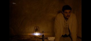 Кадр из сериала «Тутанхамон»: мужчина в тёмном помещении рядом со светильником и бутылкой, создающий атмосферу предчувствия и тревоги.
