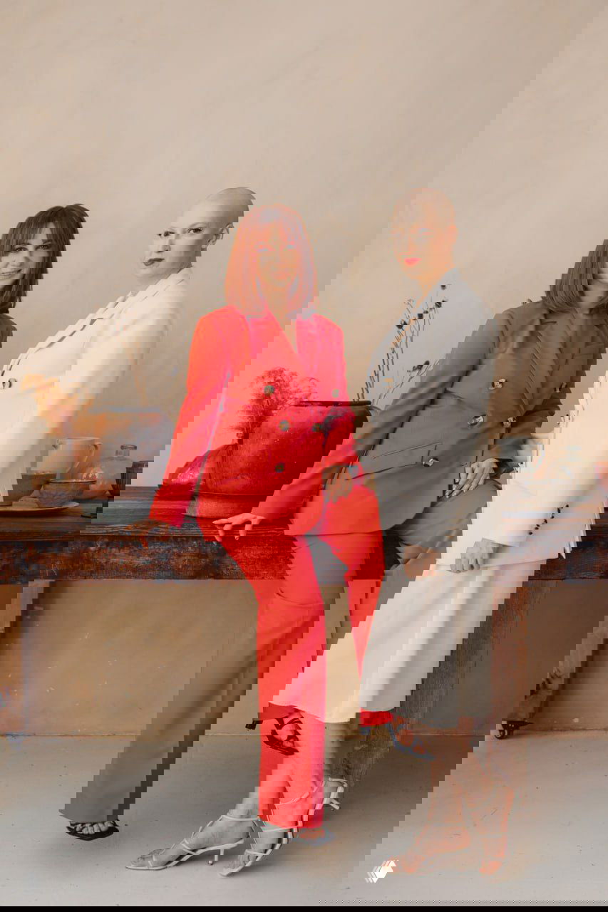 Портрет двух женщин в деловых костюмах: одна в красном, другая с бритой головой в белом — сила и красота после химиотерапии.