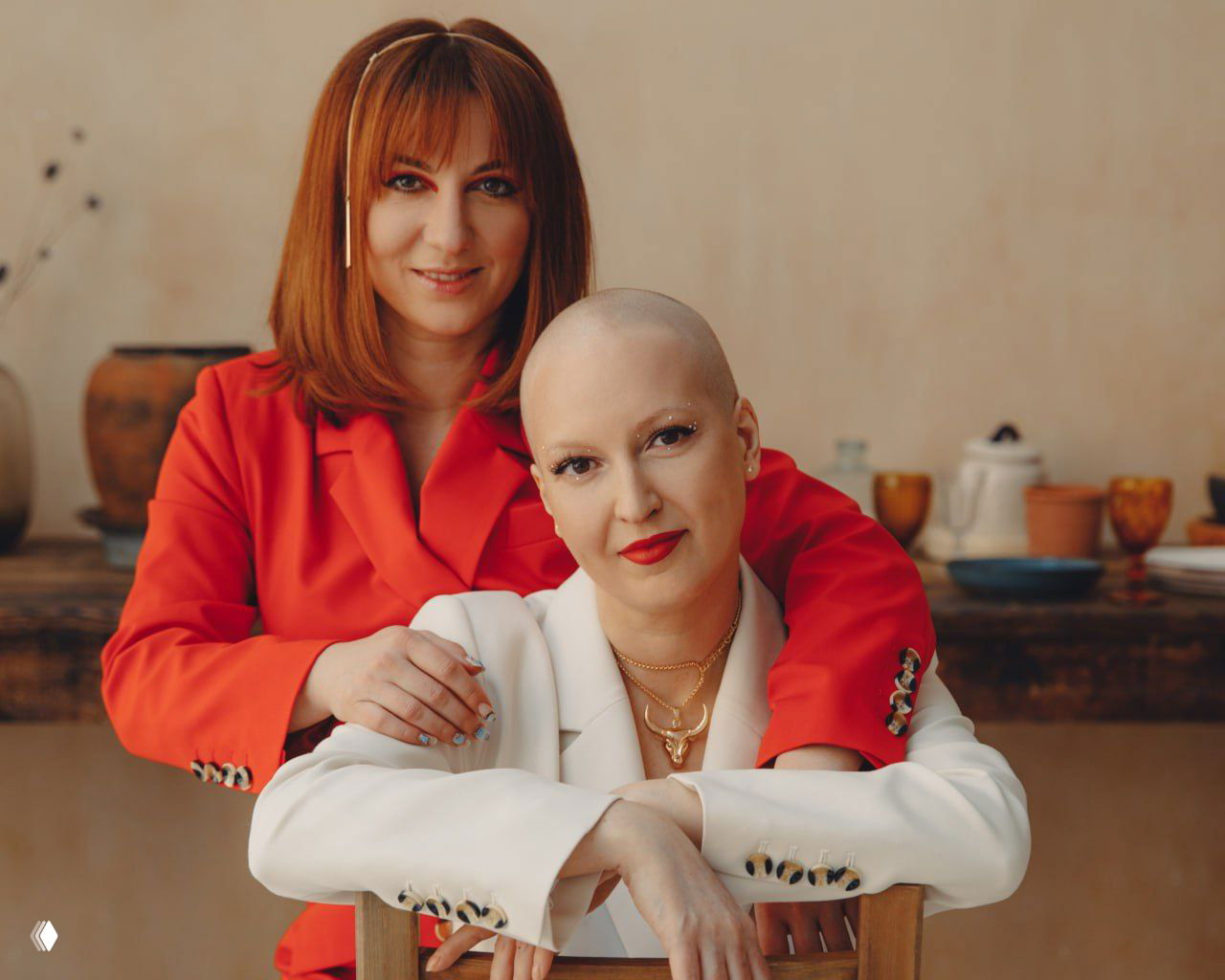 Женщины сидят и улыбаются на песке под люстрами, композиция передаёт устойчивость, дружбу и спокойное принятие после испытаний.