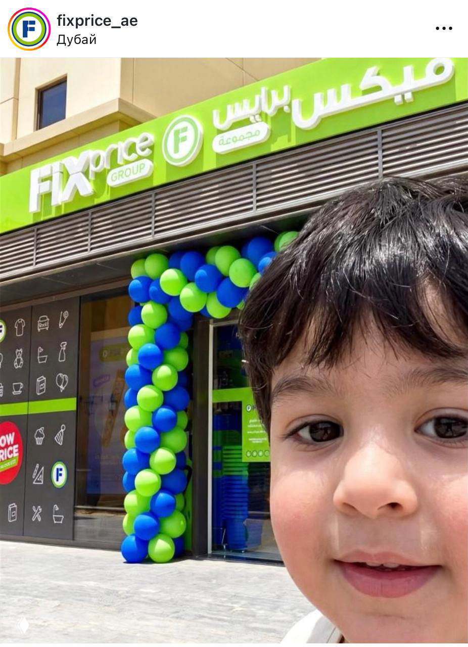 Селфи ребёнка у входа в магазин FixPrice: крупный план лица на фоне праздничного оформления фасада и шаров.