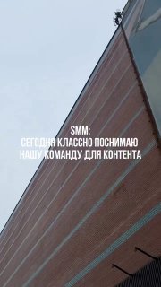Вертикальное фото фасада и крыши; на краю крыши виден человек‑оператор вдалеке, поверх изображения белый текст про SMM и съёмку команды для контента.