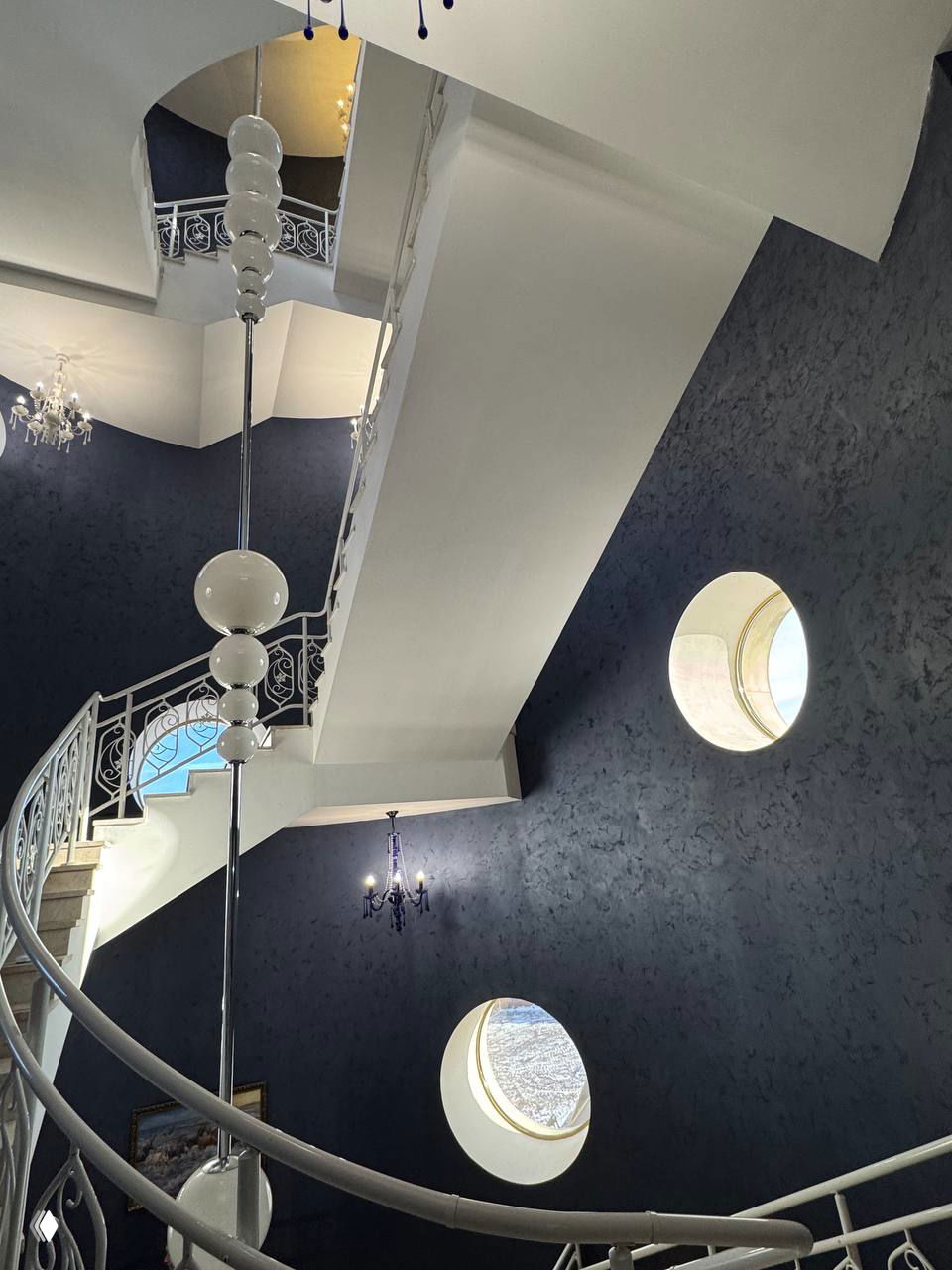 Спиральная лестница и круглые окна внутри театра, архитектурные детали и стильный интерьер, вид на несколько уровней фойе и декоративные светильники.