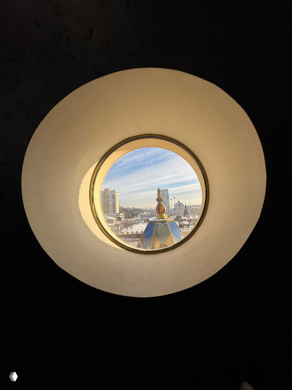 Круглое окно с видом на купол театра и город за ним, зимний пейзаж и элементы фасада видны через круглое окошко, кадр отсылает к интерьеру замка.