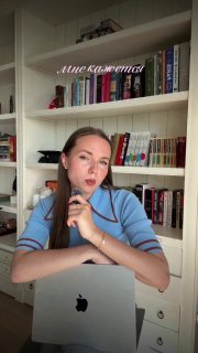 Женщина за ноутбуком на фоне книжной полки, рабочая обстановка и жест руки у подбородка; иллюстрация к подборке курсов и ресурсов.