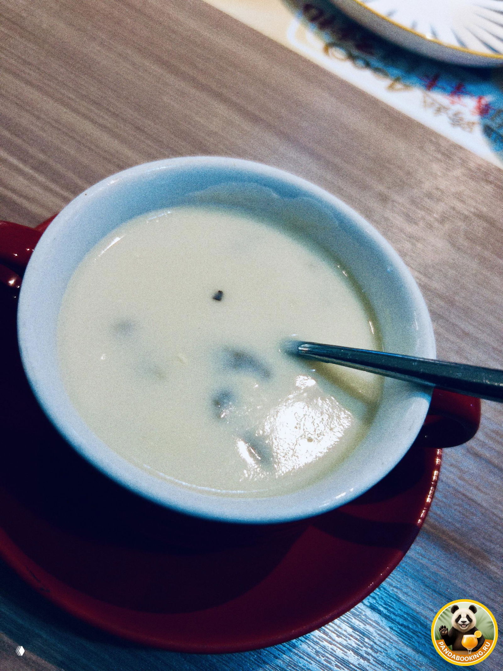 Белая чашка с кремовым супом или кофе на столе, вид сверху, в красной подставке — простая гарнировка к пицце в международной сети в Китае.