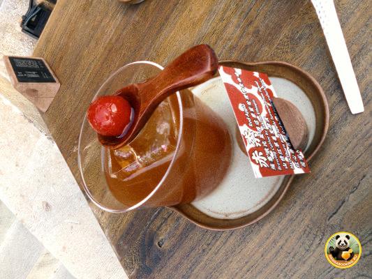 Стеклянная чашка с напитком и керамической ложкой, возможно яблочный кофе, поданная на столе с биркой и блюдцем в кафе Пекина.