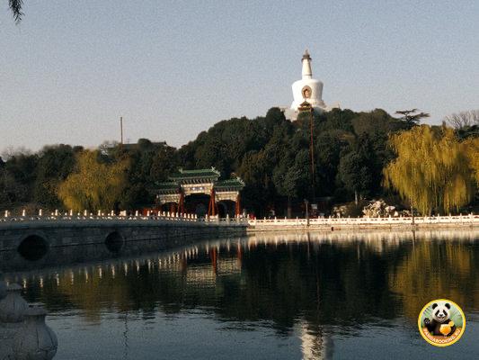 Пейзаж парка в Пекине с озером и белой пагодой на холме, отражение в воде и спокойная прогулочная атмосфера рядом с памятником.