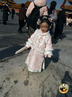 Маленькая девочка в традиционном китайском костюме на территории Запретного города, улыбается и стоит в окружении туристов.