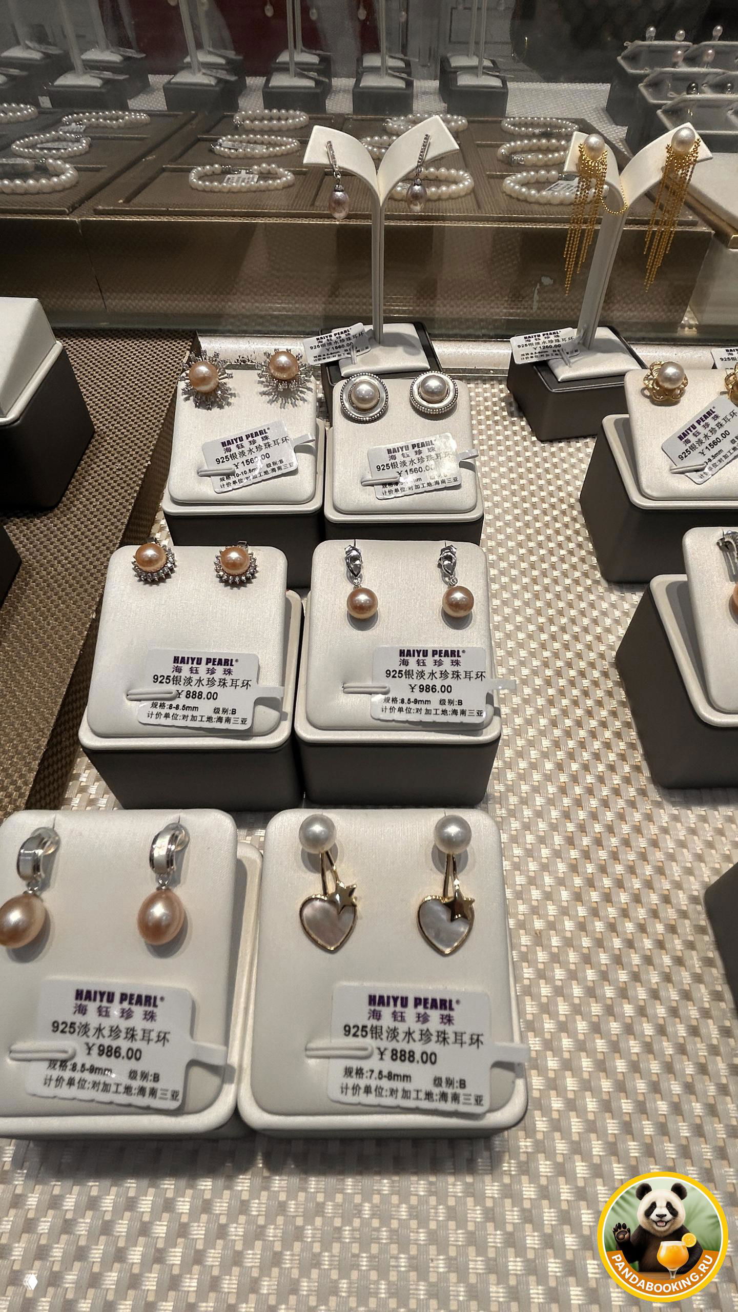 Крупный план нескольких пар жемчужных серьг и подвесок на подставках, видны ценники с указанием цены в юанях и маркировкой Haiyu Pearl.
