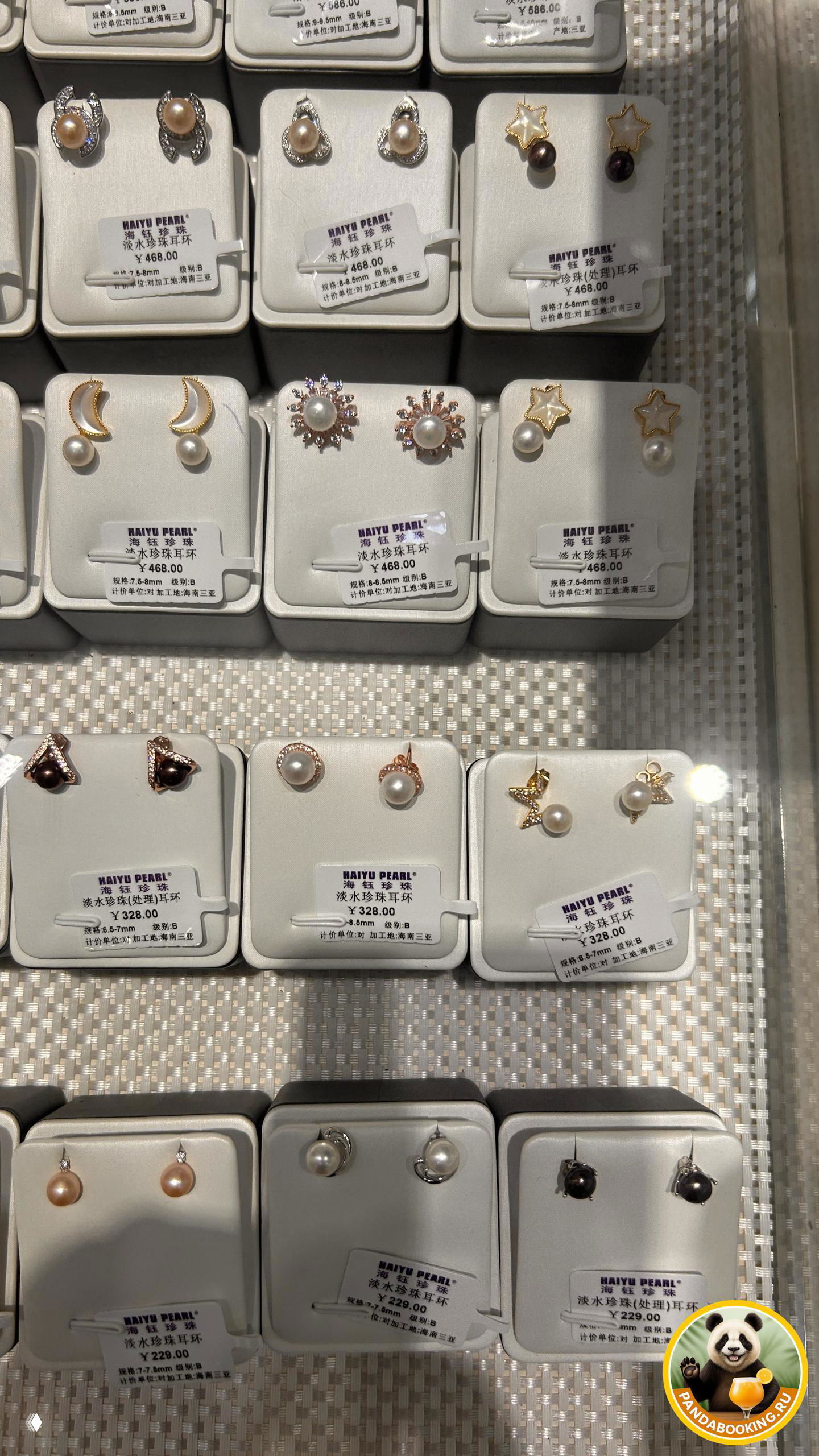 Крупные план-кадры маленьких жемчужных гвоздиков и серёжек на подставках, хорошо видно текст на ценниках и разнообразие размеров жемчуга.