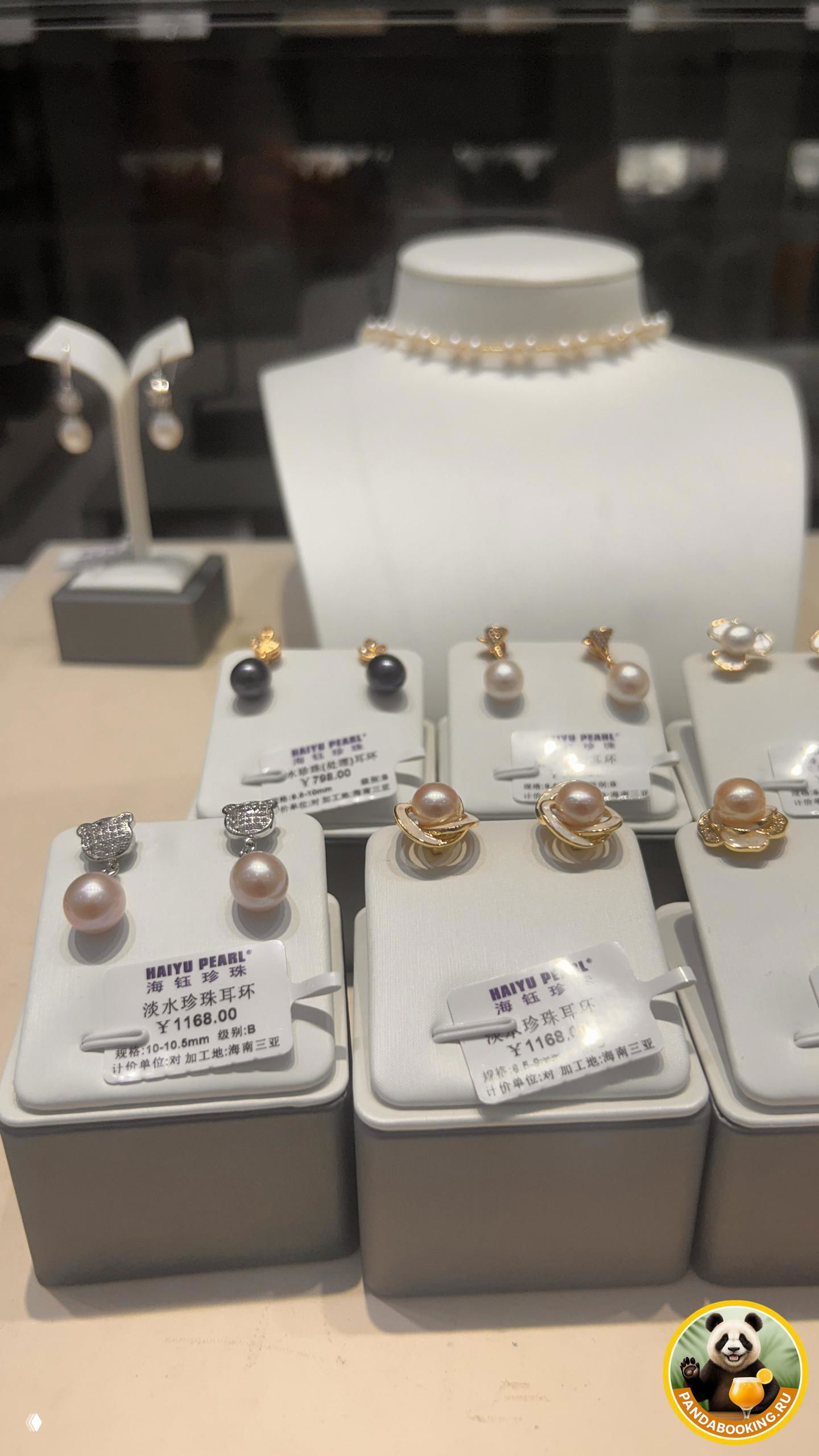 Фотография витрины с несколькими рядами подставок и подвесок, в кадре — жемчужное ожерелье на манекене и серьги на переднем плане.