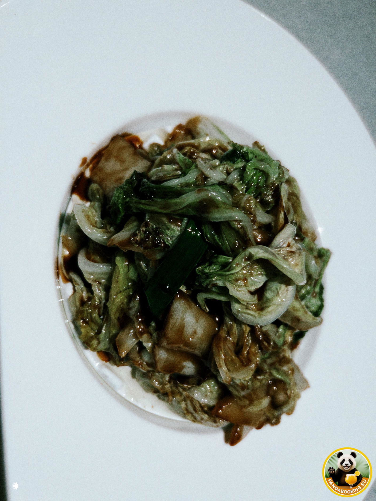 Тушёная капуста в тёмном соусе на белой глубокой тарелке — нежная текстура и тёплый оттенок заправки, подача в центре стола.