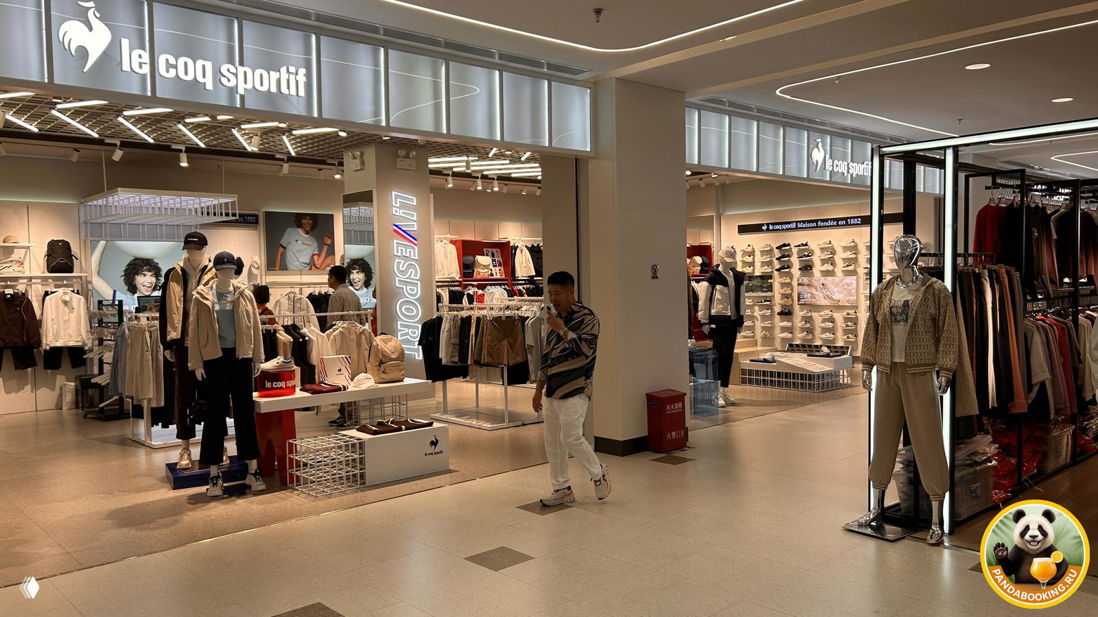 Витрина и внутренность магазина Le Coq Sportif и смежных бутиков с манекенами, вывески брендов и покупатели внутри торгового пространства.