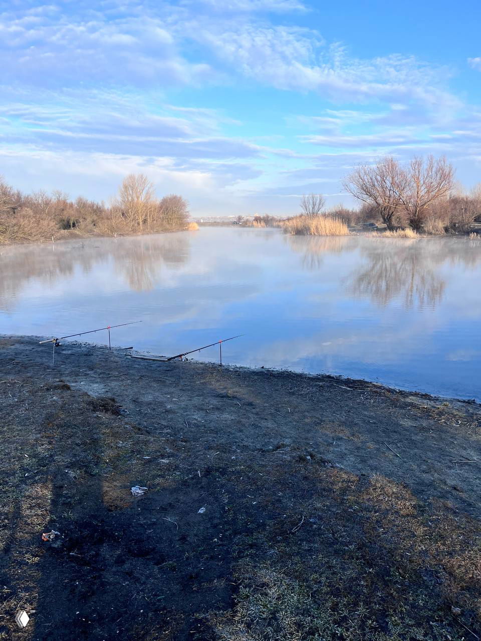 Спокойная гладь реки с отражением неба и пустыми удилищами на берегу: раннее утро и аккуратные места для ловли.