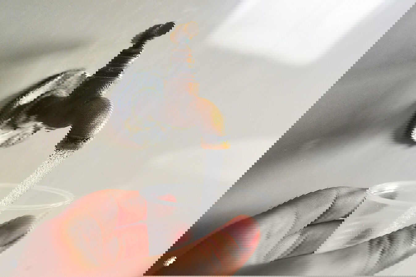 Кран с проточной водой и пластиковый стакан в руке — демонстрация доступной питьевой лечебной воды и сервиса для посетителей санатория «Эльбрус».