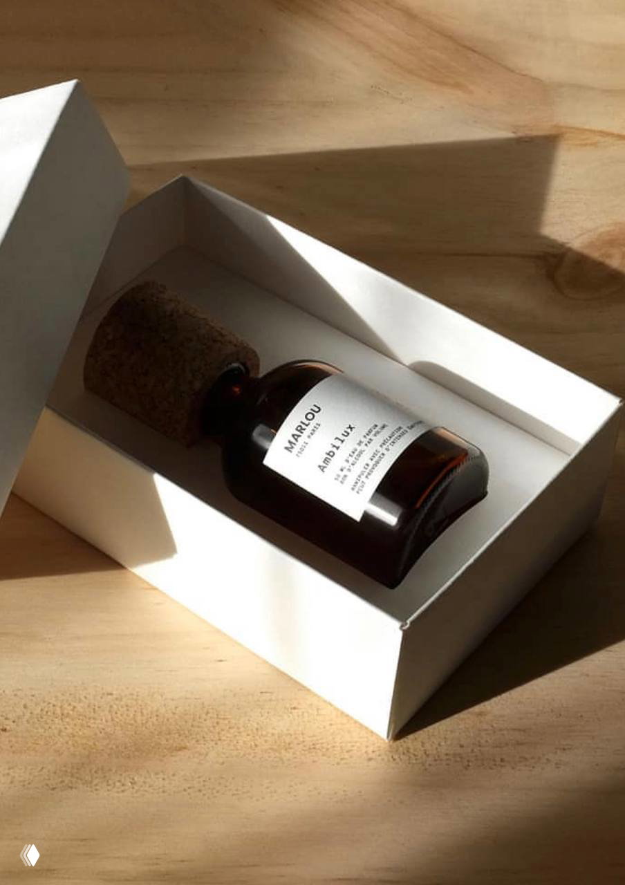 Флакон Ambilux Marlou в белой коробке на деревянной поверхности; мягкий боковой свет выделяет пробковую пробку и этикетку.