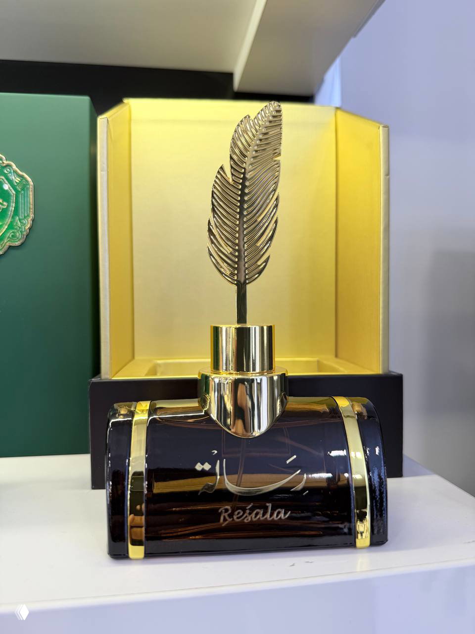 Крупный снимок флакона Resala Arabian Oud с декоративным пером-капсулой на фоне золотистой коробки, акцент на богатом дизайне и позолоте.