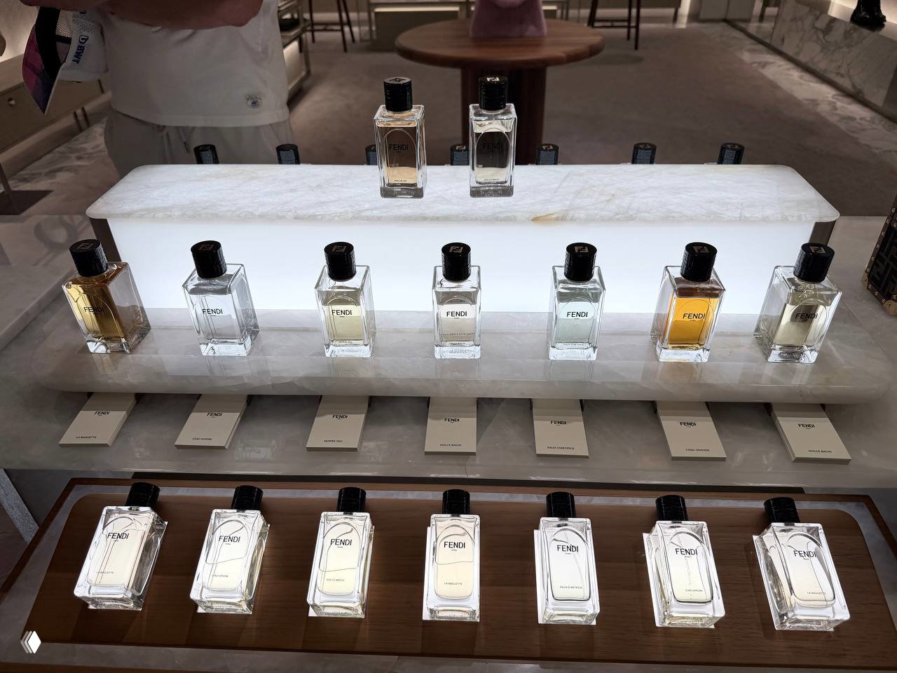 Подсвеченная экспозиция флаконов Fendi на мраморной подставке: несколько тестеров и ценников, аккуратная витрина бутика.