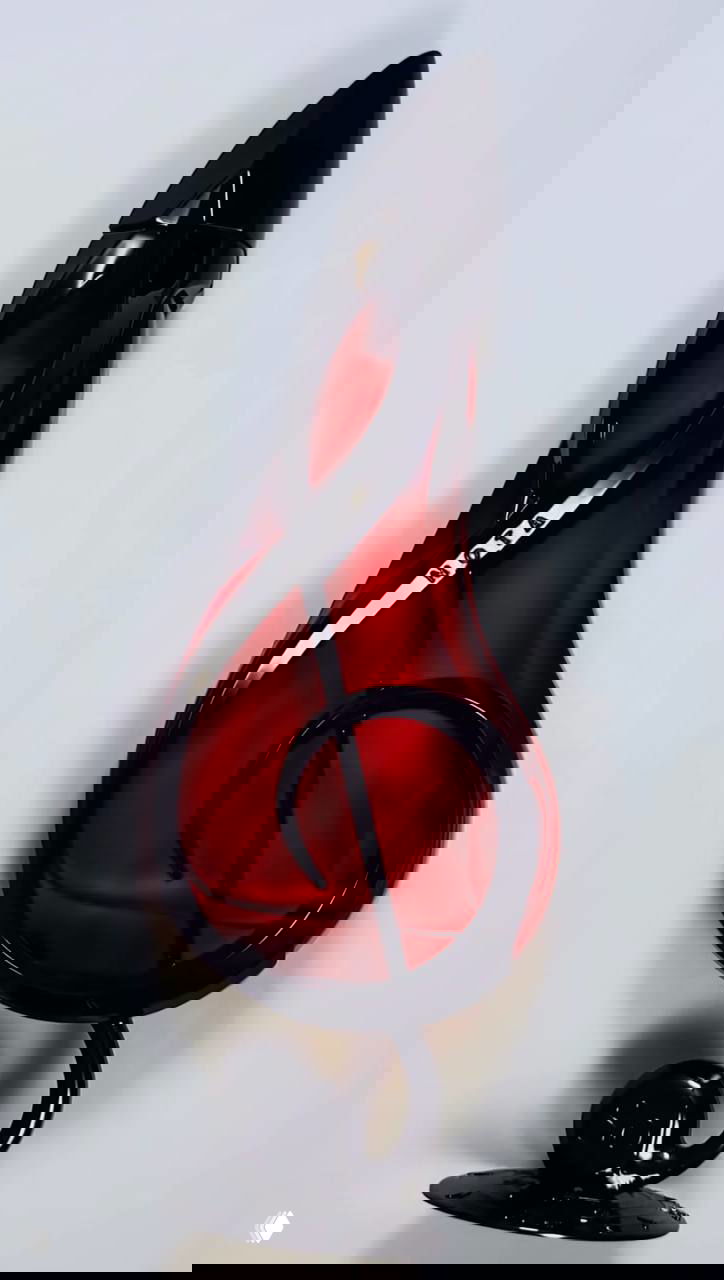 Тёмно-красный парфюмерный флакон в форме скрипичного ключа, подчеркнутый чёрными декоративными элементами и блеском стекла на белом фоне.