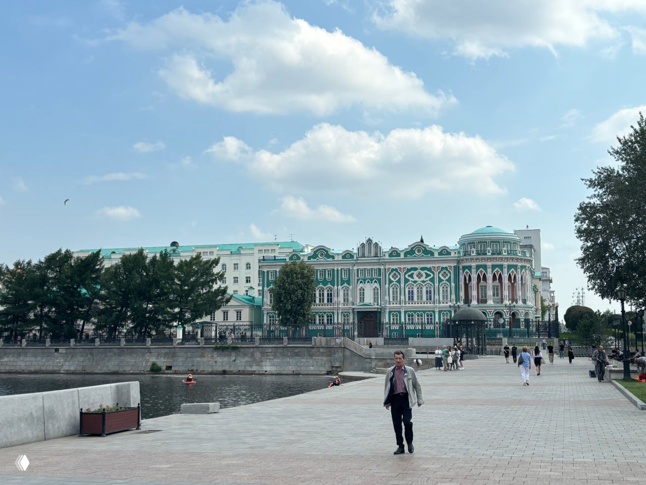 Прогулочная зона на Плотинке и зелёно-белый орнаментированный особняк (Дом Севастьянова): люди гуляют, видна набережная и река.