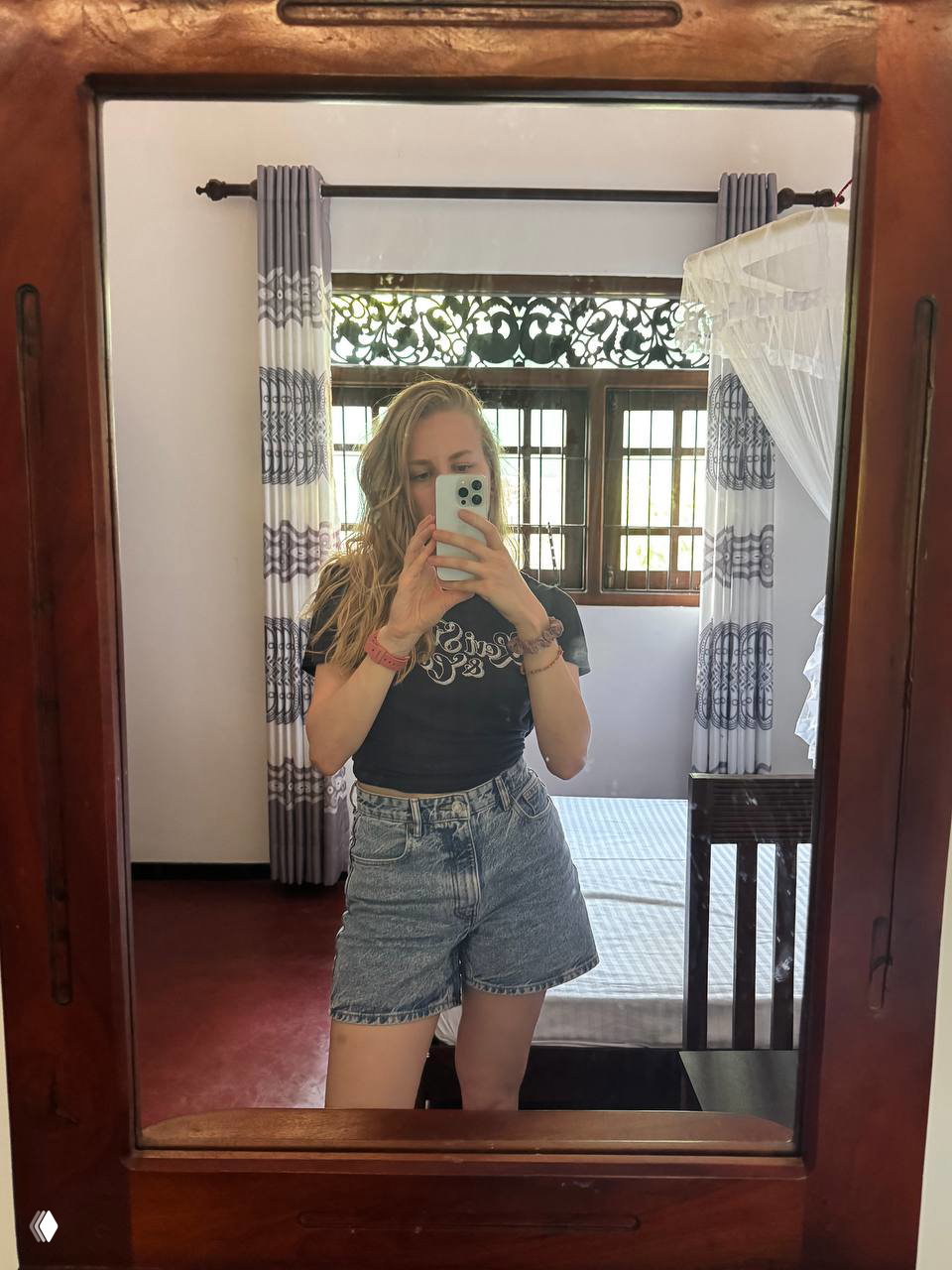 Автор делает фото в зеркале внутри комнаты с кроватью и ажурной резьбой на окне — интерьер жилья во время пребывания на Шри-Ланке.