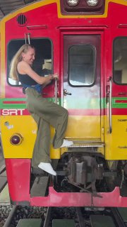 Девушка забирается на переднюю часть яркого поезда на рельсах в зоне рынка‑поезда, цветной локомотив и туристическая атмосфера вокруг. Фото автора.