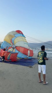Парасейлинг на пляже Дананга: подготовленный парашют и человек в футболке смотрит на море и горы на заднем плане.