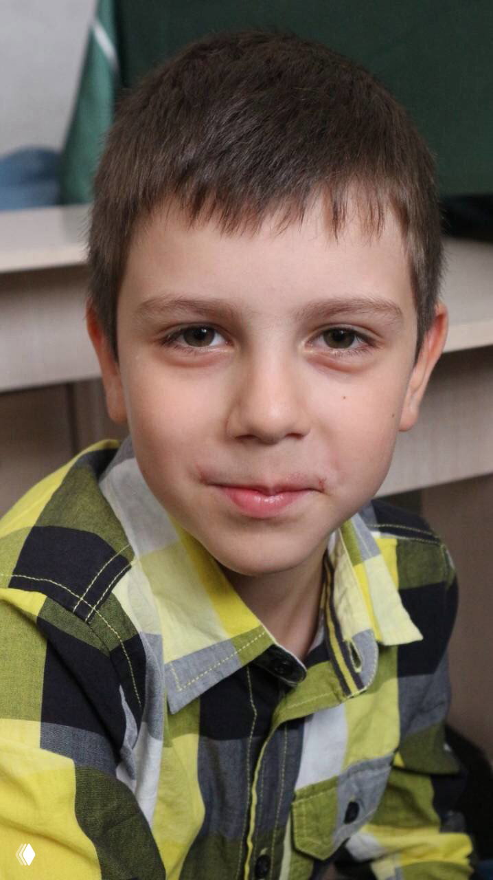 Крупный план мальчика школьного возраста с тёмными глазами и короткой стрижкой, спокойный выражение лица, вероятно портрет в комнате.