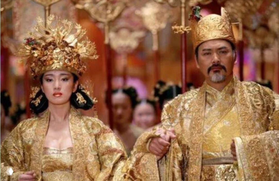 Кадр из «Проклятье золотого цветка» (2006): император и императрица в роскошных золотых убранствах на фоне дворцовой церемонии и свиты.