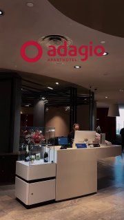 Ресепшн апарт‑отеля Adagio Москва Киевская: стойка регистрации, сотрудник у стойки и логотип Adagio на потолке в интерьере лобби.