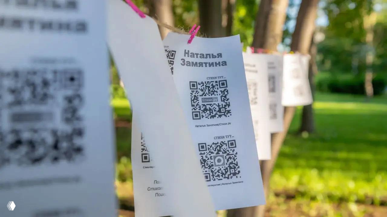 Бумажные листы с QR-кодами и печатью «Наталья Замятина», развешенные на верёвке — промо-материалы и раздатка с произведениями автора.