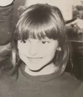 Чёрно-белая фотография улыбающейся девочки примерно восьми лет в домашней обстановке, с чёлкой и свитером; портрет автора.