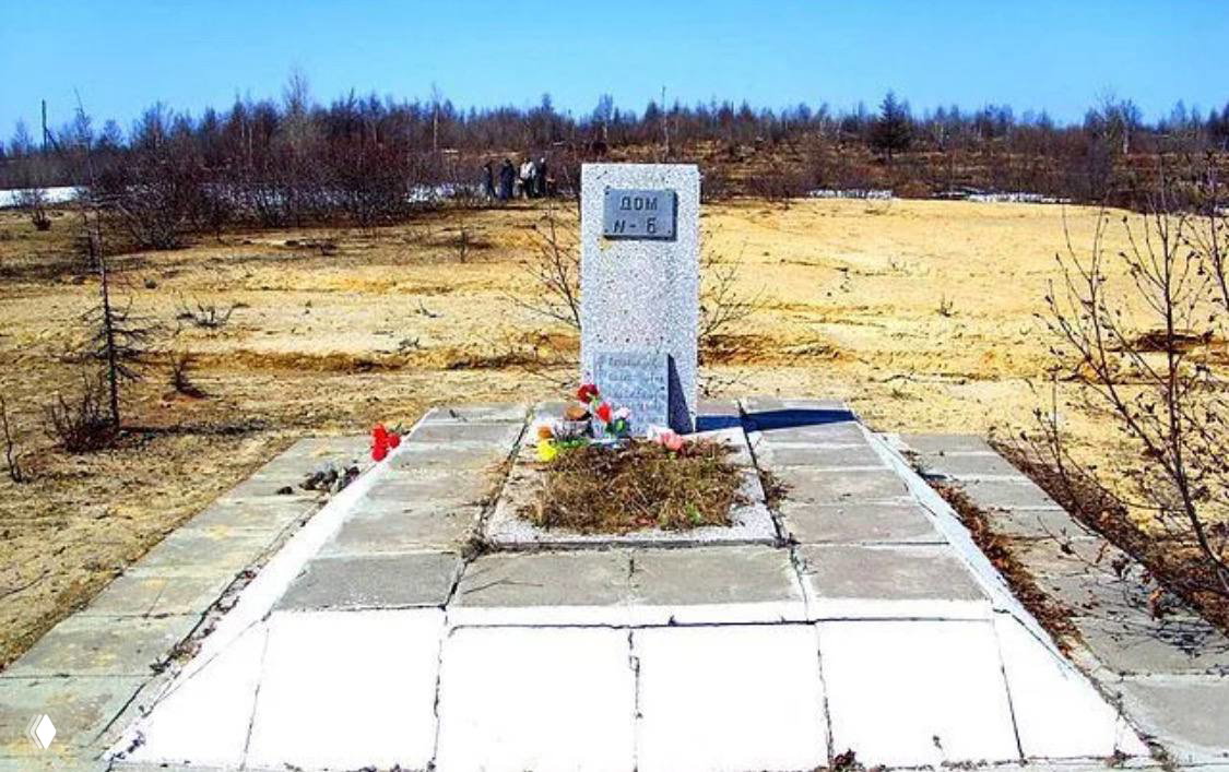 Братская могила или памятный камень на месте бывшего дома Н‑6 в урочище Нефтегорск, плита с надписью и следы цветов и лампад.