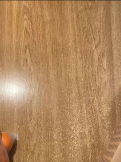 Фото пола из деревянного ламината с отражением света и частью предмета в левом нижнем углу; нейтральный фоновый кадр.