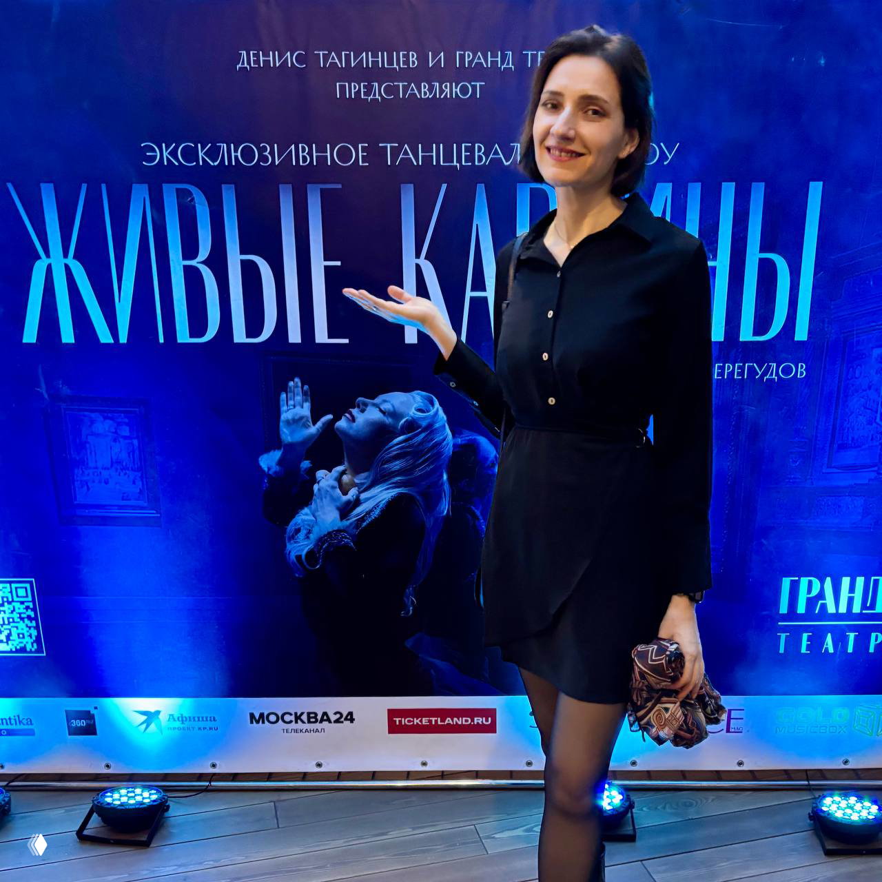 Автор канала на фоне афиши шоу «Живые картины» у входа в театр — улыбается, фотография с постером постановки и логотипами партнёров.