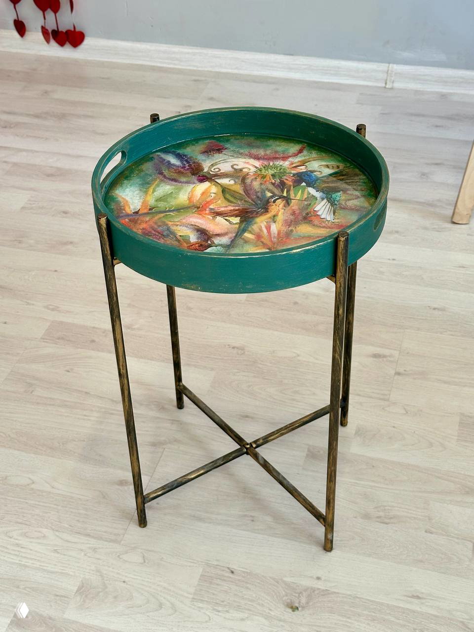 Полный вид на декоративный кофейный столик на металлических ножках: круглая подносная столешница с тропическим рисунком и зелёной окантовкой.