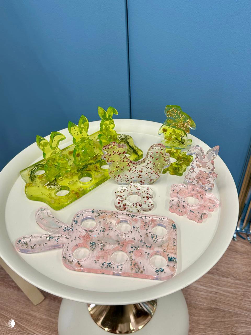 Несколько подставок для яиц из цветной и прозрачной эпоксидной смолы с блёстками и растительными вставками на белом подносе.