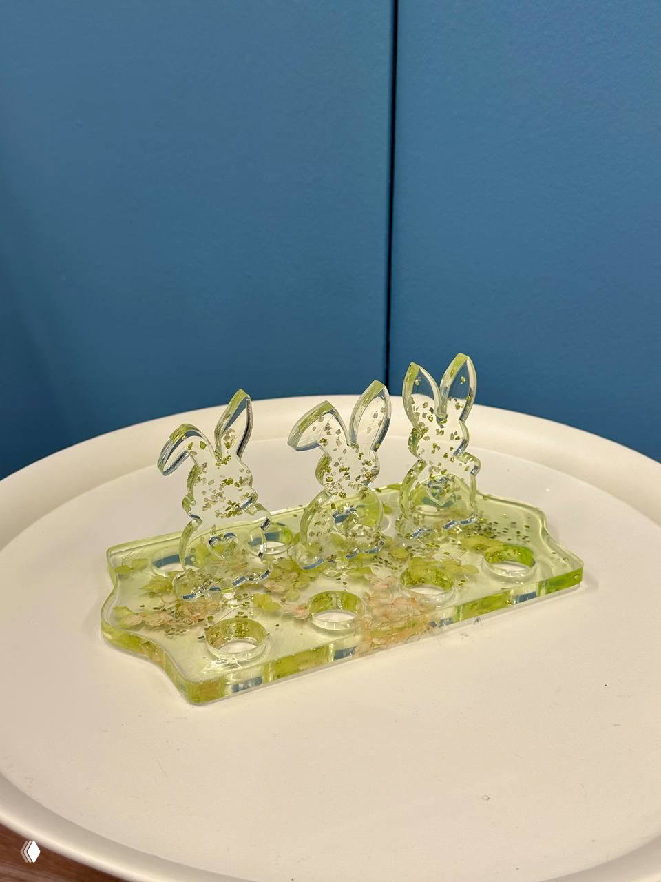 Зелёная прозрачная подставка для яиц с тремя фигурными зайчиками из эпоксидной смолы на белом подносе, крупный план.