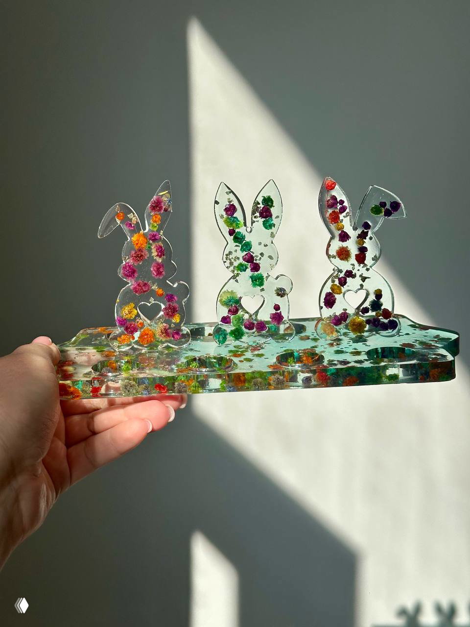 Фотография подноса из эпоксидной смолы с тремя декоративными зайцами‑фигурками и множеством цветных вкраплений, показано в солнечном контровом свете.