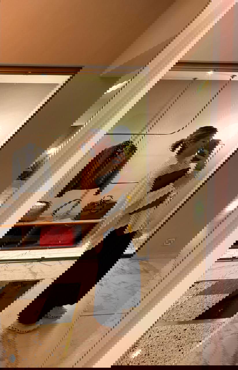 Зеркальное селфи автора в холле отеля: девушка держит планшет и ноутбук, свободная одежда и повседневный образ в интерьере бутикового отеля.