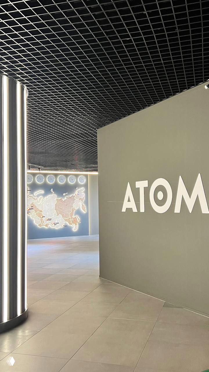 Входная зона музея с крупной надписью «ATOM» и подсвеченной картой; современный дизайн интерьера и колонна с подсветкой.
