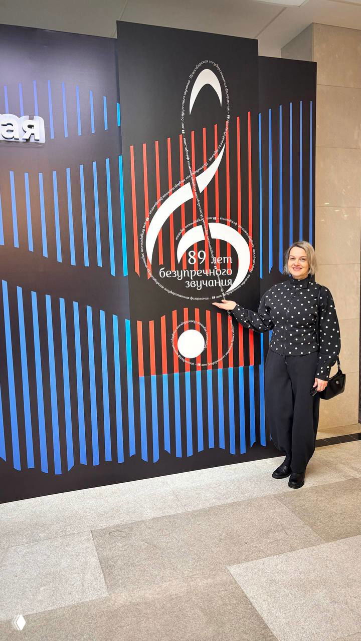 Угловой вид фасада Новосибирской филармонии с отражающими витражами и заснеженной территорией у входа, дневной кадр здания.