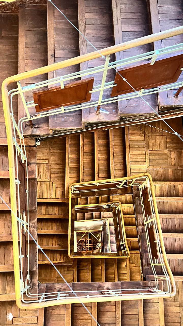 Вид сверху на винтовую деревянную лестницу музея с многочисленными пролётами и перилами — геометрия и фактура интерьера старого здания.