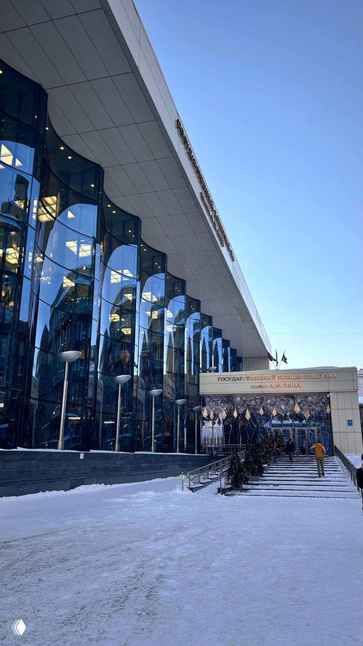 Главный вход филармонии с украшениями и подсветкой, заснеженные ступени и люди, поднимающиеся к дверям концертного зала.