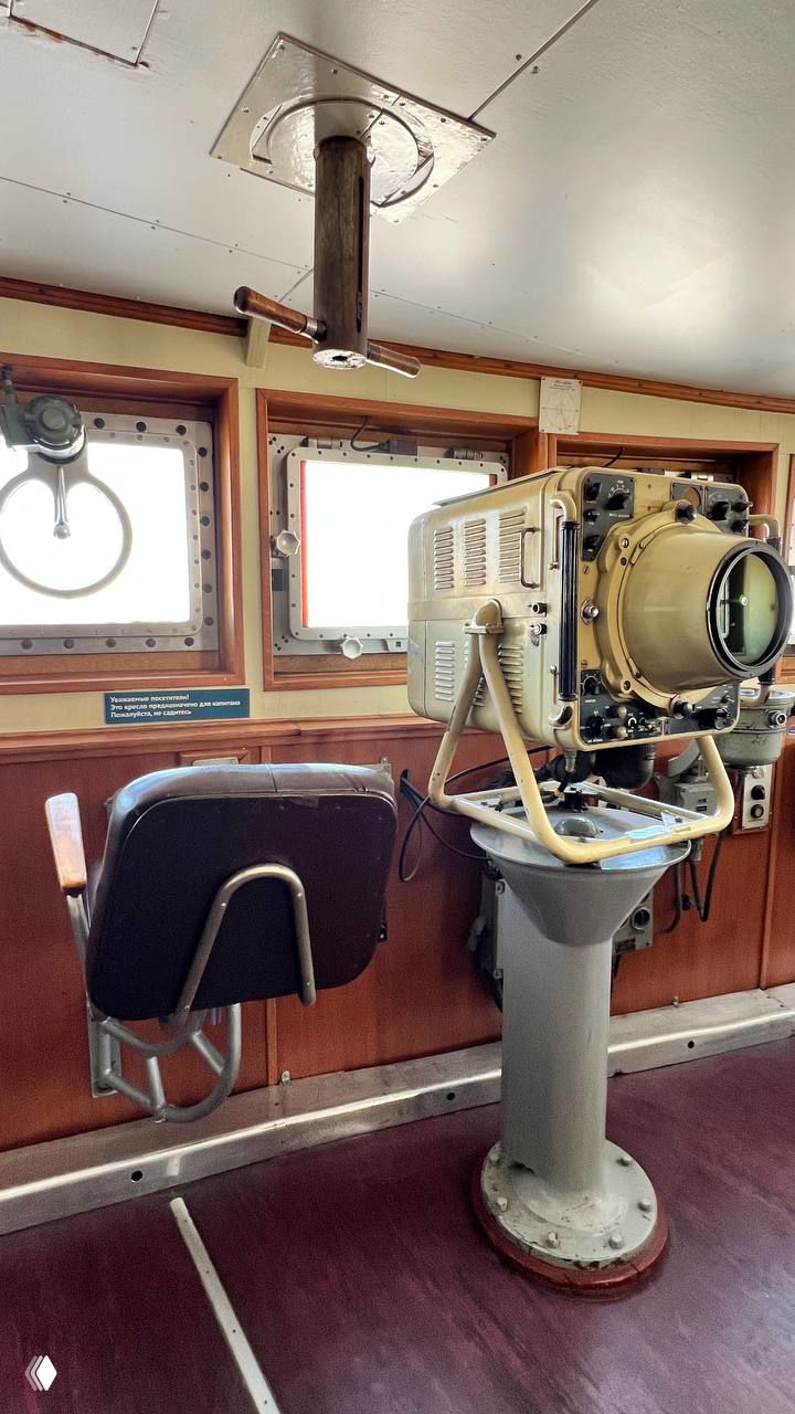 Вид из рубки: навигационная аппаратура и приборы на фоне иллюминаторов, деревянная отделка и кресло оператора — интерьер рабочего места судна.