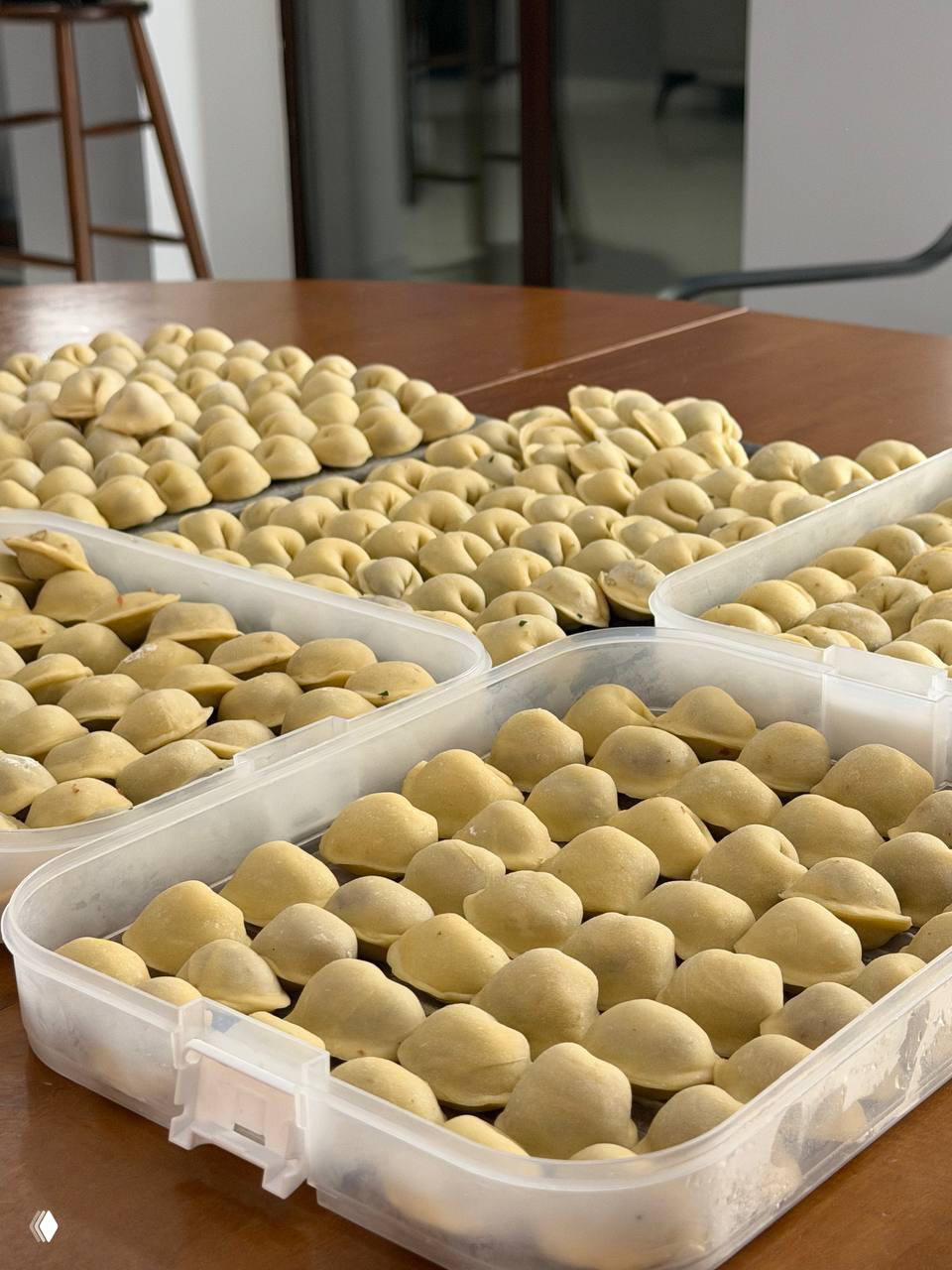 Пластиковые контейнеры, плотно заполненные рядами неварёных круглых пельменей — аккуратно выложенные заготовки, готовые к заморозке или варке.